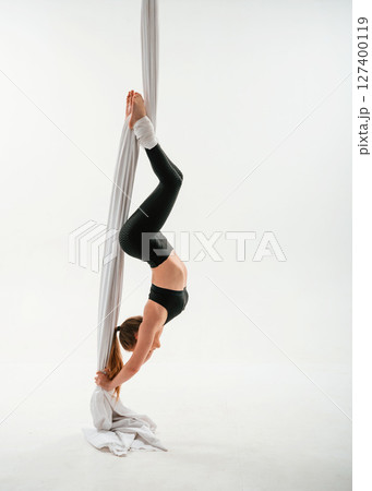 Hanging upside down. Young beautiful woman doing fly yoga against white background 127400119