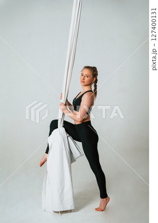 In black sportswear, stretching. Young beautiful woman doing fly yoga against white background In black sportswear, stretching. Young beautiful woman doing fly yoga against white background 127400131