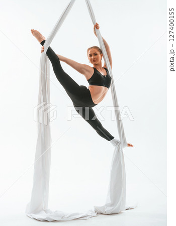 Stretching the legs. Young beautiful woman doing fly yoga against white background 127400155