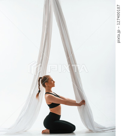 Sitting, holding canvas, side view. Young beautiful woman doing fly yoga against white background 127400187