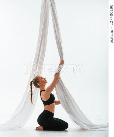 Sitting, holding canvas, side view. Young beautiful woman doing fly yoga against white background Sitting, holding canvas, side view. Young beautiful woman doing fly yoga against white background 127400190