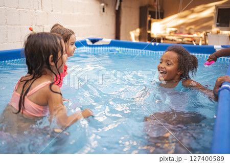 Children play joyfully in a backyard pool during summer afternoon 127400589