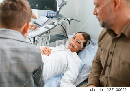 Son and husband are supporting mother. Pregnant woman is lying down in the hospital, doctor does ultrasound 127400631