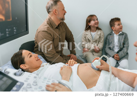 Family is sitting together. Pregnant woman is lying down in the hospital, doctor does ultrasound 127400669