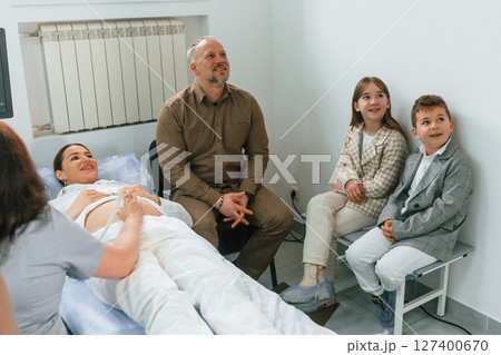 Family is sitting together. Pregnant woman is lying down in the hospital, doctor does ultrasound Family is sitting together. Pregnant woman is lying down in the hospital, doctor does ultrasound 127400670