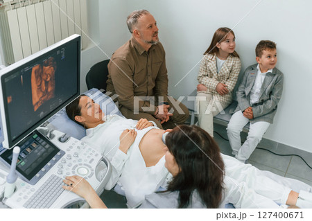 Family is sitting together. Pregnant woman is lying down in the hospital, doctor does ultrasound Family is sitting together. Pregnant woman is lying down in the hospital, doctor does ultrasound 127400671