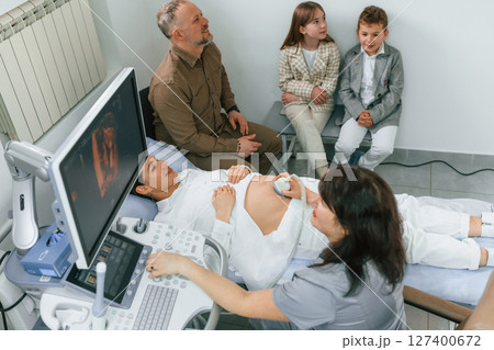 Family is sitting together. Pregnant woman is lying down in the hospital, doctor does ultrasound 127400672