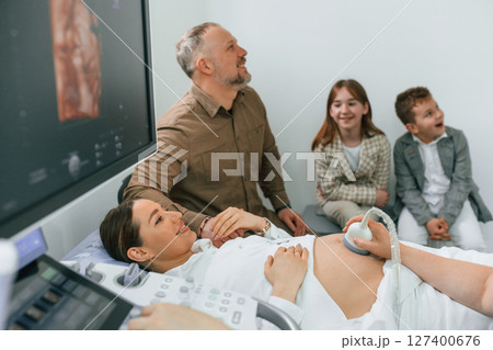 Husband and kids are sitting together. Pregnant woman is lying down in the hospital, doctor does ultrasound 127400676