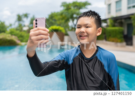 Asian teenage boy using phone after swimming in pool 127401150