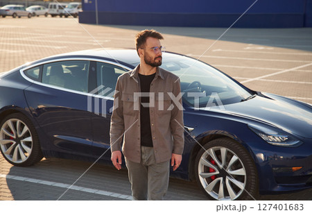 In glasses. Man is standing near his electric car outdoors 127401683