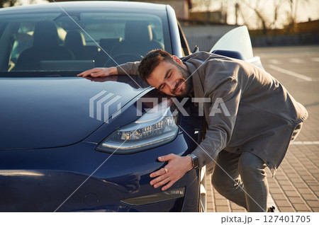 Embracing the automobile. Man is standing near his electric car outdoors Embracing the automobile. Man is standing near his electric car outdoors 127401705
