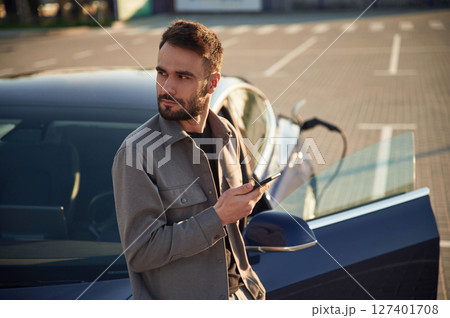 Charging the automobile. Man is standing near his electric car outdoors Charging the automobile. Man is standing near his electric car outdoors 127401708