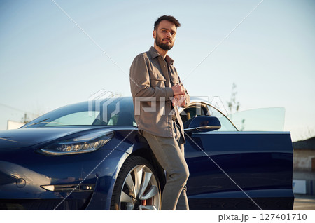 Charging the automobile. Man is standing near his electric car outdoors Charging the automobile. Man is standing near his electric car outdoors 127401710