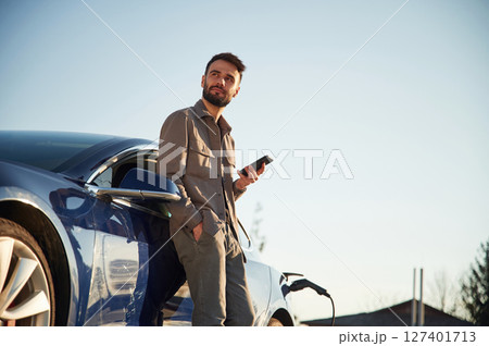 Man is standing near his electric car outdoors Man is standing near his electric car outdoors 127401713
