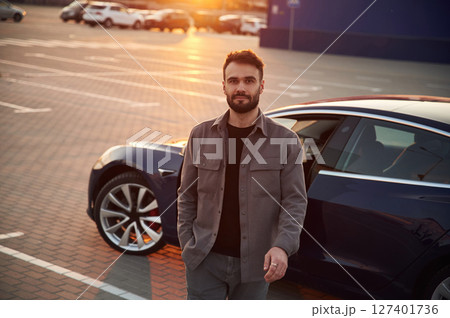 Sunny background. Man is standing near his electric car outdoors 127401736