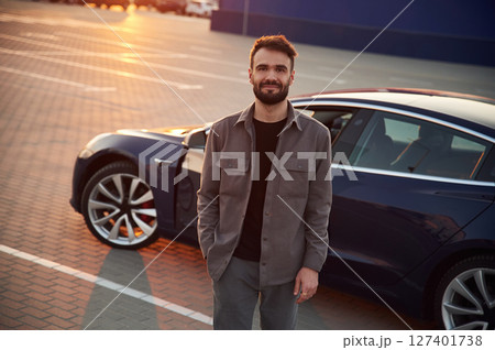 Sunny background. Man is standing near his electric car outdoors Sunny background. Man is standing near his electric car outdoors 127401738