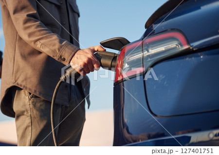 Conception of green energy. Man is standing near his electric car outdoors Conception of green energy. Man is standing near his electric car outdoors 127401751