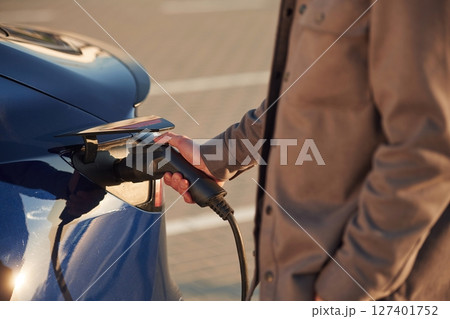 Conception of green energy. Man is standing near his electric car outdoors Conception of green energy. Man is standing near his electric car outdoors 127401752