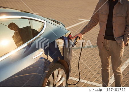 Beautiful yellow sunlight. Man is standing near his electric car outdoors 127401755
