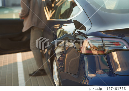 Rear part of the automobile that is charging. Man is standing near his electric car outdoors Rear part of the automobile that is charging. Man is standing near his electric car outdoors 127401758
