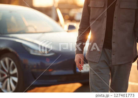 Bright sunlight. Man is standing near his electric car outdoors Bright sunlight. Man is standing near his electric car outdoors 127401773