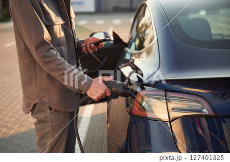 In formal clothes. Man is standing near his electric car outdoors 127401825
