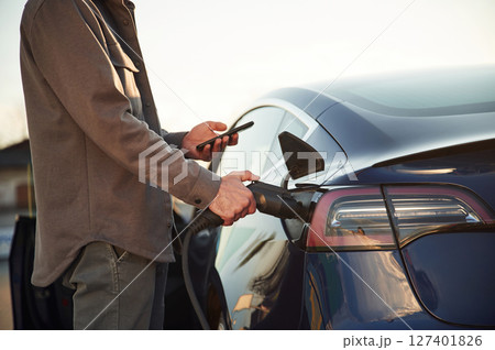 Grey colored formal clothes. Man is standing near his electric car outdoors 127401826
