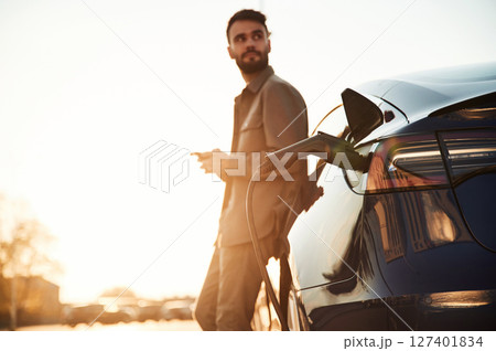 In the beautiful sunlight. Man is standing near his electric car outdoors 127401834