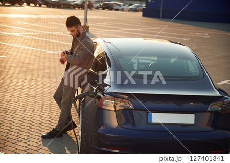 On the charging station. Man is standing near his electric car outdoors On the charging station. Man is standing near his electric car outdoors 127401841