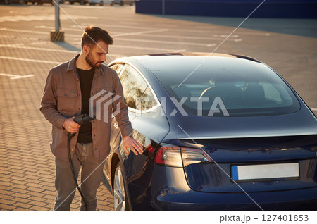Back view of the automobile. Man is standing near his electric car outdoors Back view of the automobile. Man is standing near his electric car outdoors 127401853