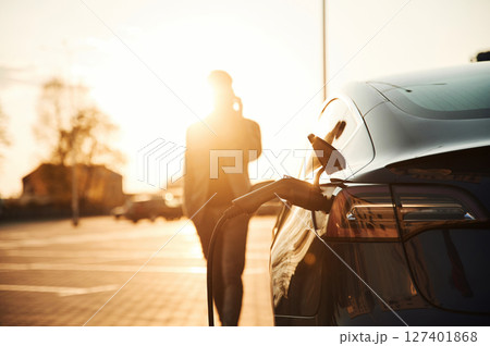 Talking by phone. Man is standing near his electric car outdoors Talking by phone. Man is standing near his electric car outdoors 127401868