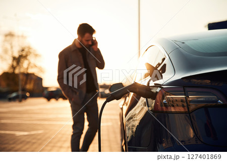 Waiting for the automobile to charge. Man is standing near his electric car outdoors 127401869