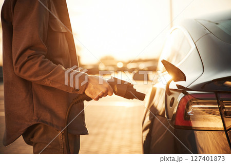 Focused close up view of the charger. Man is standing near his electric car outdoors 127401873