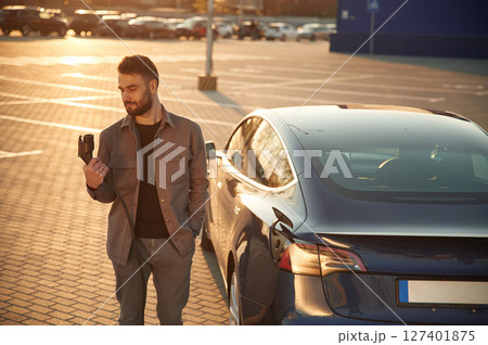 Waiting for the automobile to charge. Man is standing near his electric car outdoors Waiting for the automobile to charge. Man is standing near his electric car outdoors 127401875