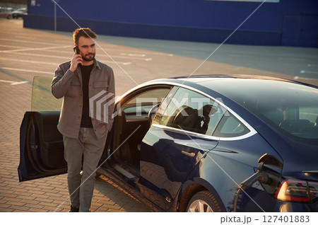 Business call by phone. Man is standing near his electric car outdoors 127401883
