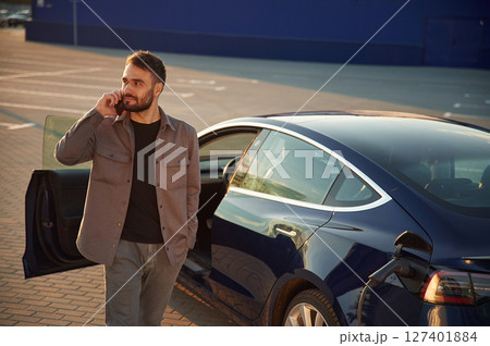 Business call by phone. Man is standing near his electric car outdoors 127401884