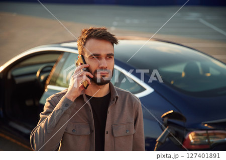 Having a call while automobile is charging. Man is standing near his electric car outdoors 127401891