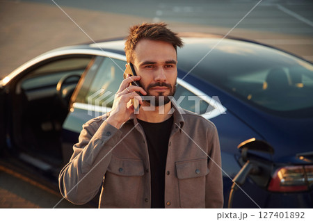 Having a call while automobile is charging. Man is standing near his electric car outdoors 127401892