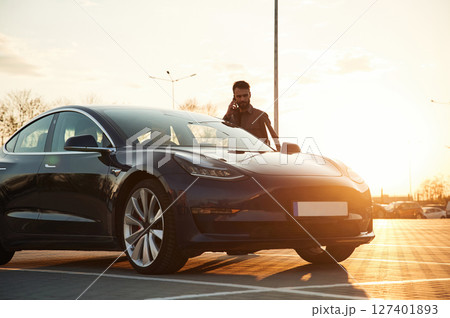 Beautiful sunlight. Man is standing near his electric car outdoors 127401893