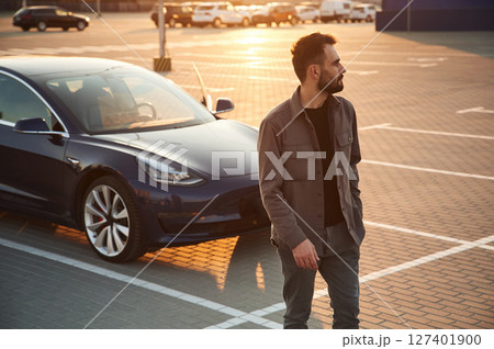Handsome man is standing near his electric car outdoors Handsome man is standing near his electric car outdoors 127401900