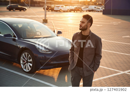 Evening time. Beautiful sunlight. Man is standing near his electric car outdoors 127401902