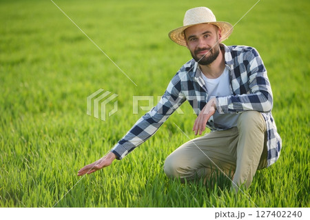 Bearded handsome young man in checkered shirt is on agricultural field Bearded handsome young man in checkered shirt is on agricultural field 127402240