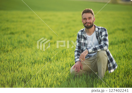 Bearded handsome young man in checkered shirt is on agricultural field Bearded handsome young man in checkered shirt is on agricultural field 127402241
