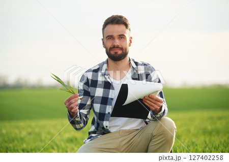 Portrait, looking at camera, holding wheat. Handsome young man is on agricultural field 127402258