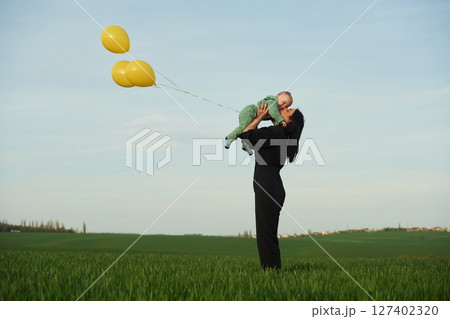 With yellow colored balloons. Mother with her little baby son is outdoors on the agricultural field 127402320