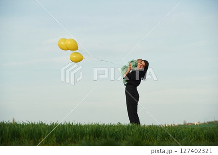 With yellow colored balloons. Mother with her little baby son is outdoors on the agricultural field 127402321