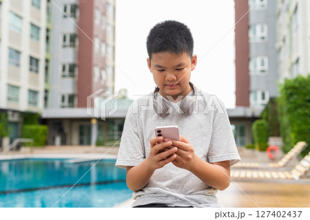 Teenage Boy at Poolside During Summer Using Phone 127402437