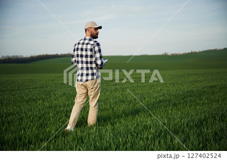 Walking, holding notepad. Handsome young man is on agricultural field 127402524
