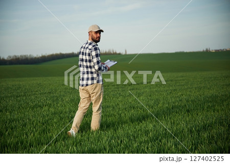 Walking, holding notepad. Handsome young man is on agricultural field 127402525