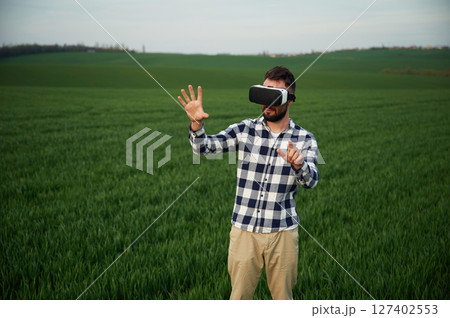 Playing game in VR glasses. Handsome young man is on agricultural field 127402553